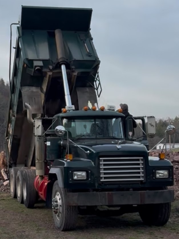 Green Mack tri-axle with the box raised, dumping a load